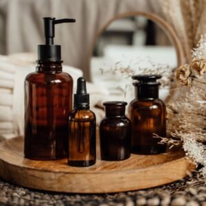 Stylish skincare setup featuring glass bottles on a wooden tray with dried flowers and towels.